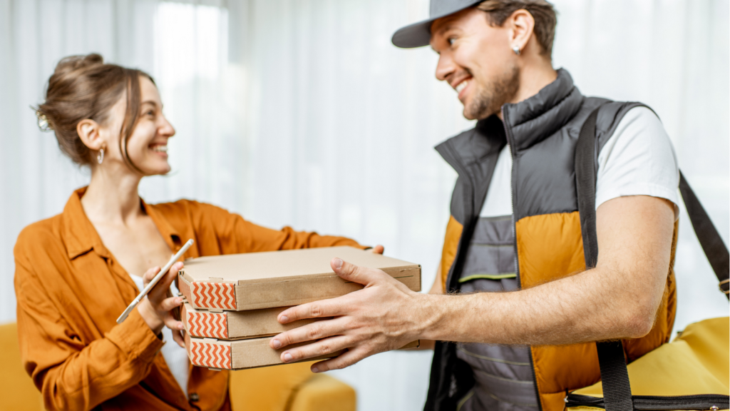 Kurier dostarcza jedzenie (pizza) kobiecie trzymającej smartfon
